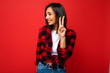 Photo of young positive happy smiling beautiful woman with sincere emotions wearing stylish clothes isolated over background with copy space and showing peace gesture