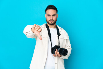 Young photographer man isolated on blue background showing thumb down with negative expression