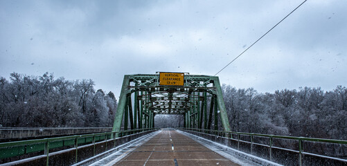 Green support bridge on two lane road during winter storm with ice and snow