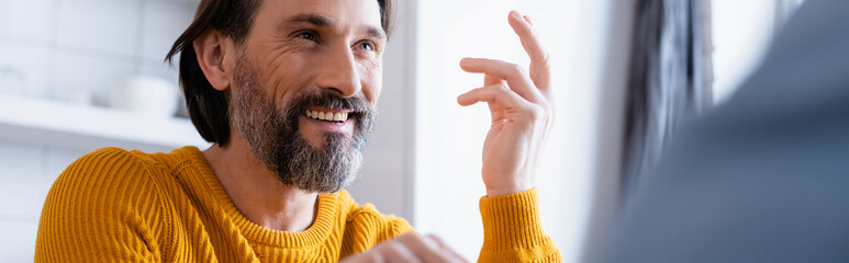 Obraz premium cheerful bearded man smiling and gesturing at home on blurred foreground, banner