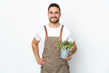 Gardener man holding a plant isolated on white background posing with arms at hip and smiling