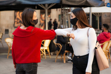 Elbow bump greeting of two women with protective face masks in city center