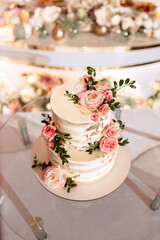 The wedding cake. White, two-tiered, decorated with flowers and gold. On a delicate pink background. Side view, top.