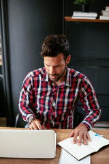 Businessman taking a notes while working on laptop. Young businessman writing in a notebook