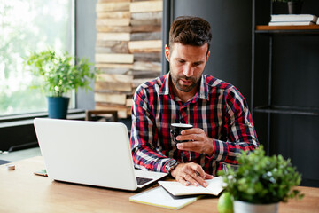 Businessman taking a notes while working on laptop. Young businessman writing in a notebook