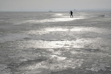 Fototapeta na wymiar Frozen sea with ice floes is shiny in sun as silver. Silhouette of person on ice. Oslonino, Gizdepka, Puck Bay, Poland
