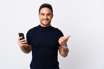 Young caucasian man using mobile phone isolated on white background pointing to the side to present...