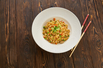 Fried rice with vegetables and beef in white plate, chopsticks on wooden background, Asian food concept, top view copy space