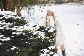 Child in a knited hat. Little girl plays with snow.