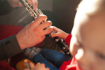 A child with his father learns to play a musical wind instrument