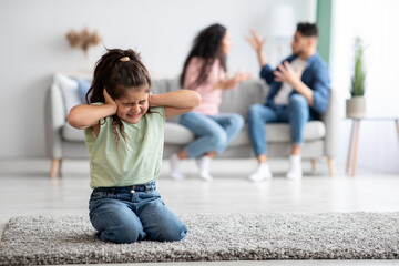 Little arabic girl covering ears with hands while parents arguing on background