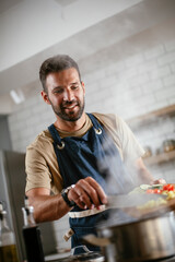  Young man cooking in the kitchen. Happy man preparing delicious food at home..