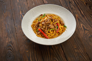 Delicious and spicy homemade noodle in white plate with black chopsticks on wooden table, asian food concept copy space for menu design