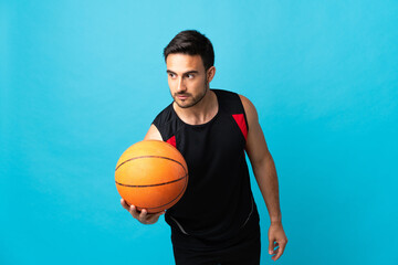 Young handsome man isolated on blue background playing basketball
