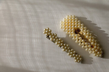 Two pearl hair clips on white background, illuminated by sunlight. Top view.