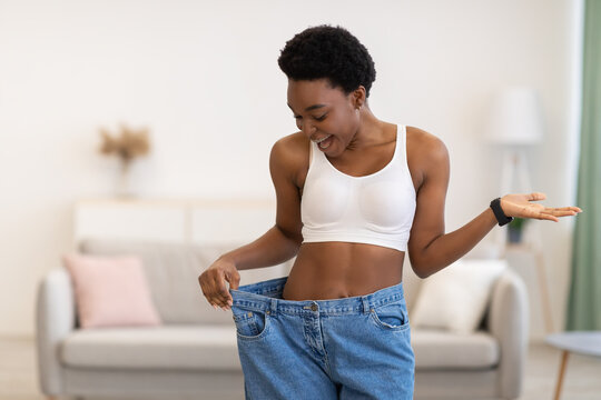 Excited Slim African Woman Wearing Oversized Pants After Weight-Loss Indoor