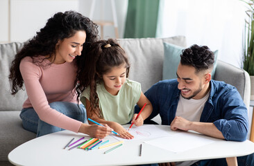Young arabic parents and their cute little daughter drawing together at home