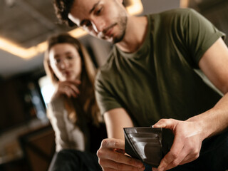 Young man checking empty wallet, no money. Unemployed sad man sitting at home showing empty wallet..