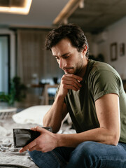 Young man checking empty wallet, no money. Unemployed sad man sitting at home showing empty wallet..