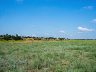Natural background. Across the entire frame in the center is a village on a high bank above it is a blue sky with white clouds, in the lower part is a large meadow with roseate grass.
