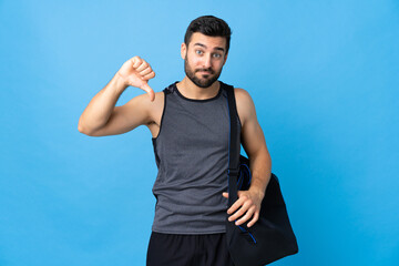 Young sport man with sport bag isolated on blue background showing thumb down with negative...