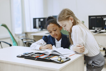Obraz premium African girl sitting at the table. Schoolgirls read a book during a break. Children sit in a computer science class.