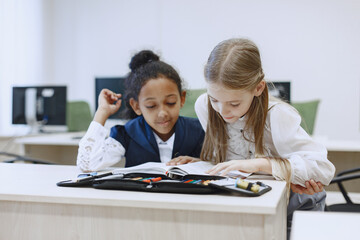 African girl sitting at the table. Schoolgirls read a book during a break. Children sit in a computer science class.