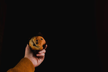 Top view closeup of a person's hand holding a chocolate chip muffin on a black background