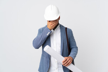 Young architect man with helmet and holding blueprints isolated on white background with tired and...