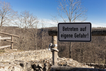 nameplate "Betreten auf eigene Gefahr!" sign with the inscription on the background of the park and ruins
