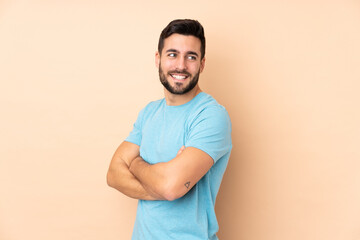 Caucasian handsome man isolated on beige background with arms crossed and happy