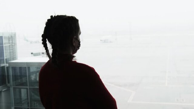 Silhouette of a Masked Young Woman at Airport Terminal Window Looking at Planes