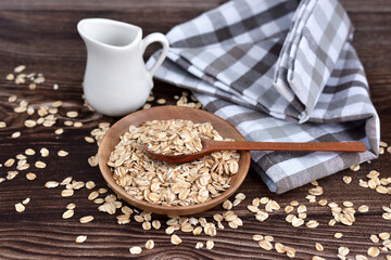 Oat flakes uncooked in wooden bowl with spoon on a dark wooden table. Concept of healthy eating