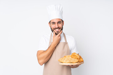 Male baker holding a table with several breads isolated on white background laughing