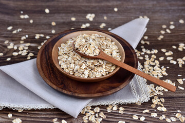 Oat flakes uncooked in wooden bowl with spoon on a dark wooden table. Concept of healthy eating