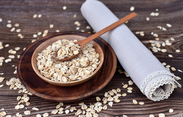 Oat flakes uncooked in wooden bowl with spoon on a dark wooden table. Concept of healthy eating