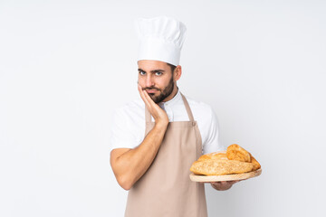 Male baker holding a table with several breads isolated on white background unhappy and frustrated