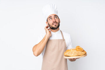 Male baker holding a table with several breads isolated on white background thinking an idea