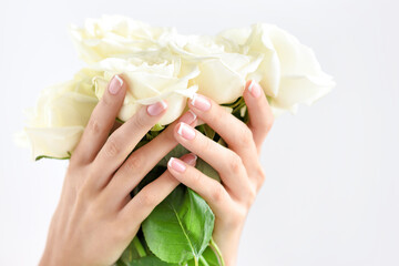 Hands of a woman with beautiful french manicure and bouquet of white roses