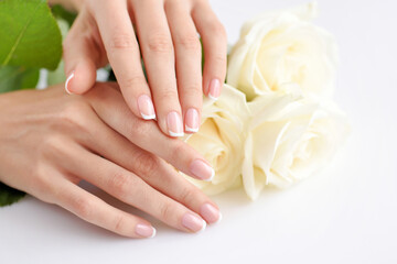 Fototapeta premium Hands of a woman with beautiful french manicure and white roses