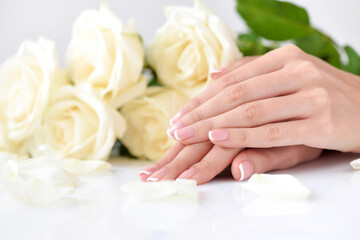 Obraz na płótnie Canvas Hands of a woman with beautiful french manicure and white roses