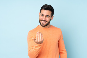 Caucasian handsome man inviting to come with hand. Happy that you came over isolated blue background