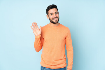 Caucasian handsome man saluting with hand with happy expression over isolated blue background © luismolinero