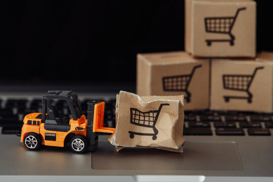 Orange forklift model and broken carton box on a keyboard close-up. Courier service and shipment accident concept.