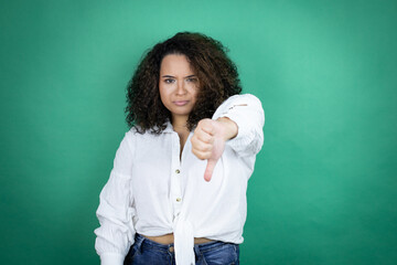 Young african american girl wearing white shirt over green background with angry face, negative...
