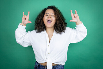 Young african american girl wearing white shirt over green background shouting with crazy expression doing rock symbol with hands up
