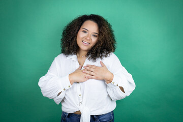 Young african american girl wearing white shirt over green background smiling with her hands on her chest and grateful gesture on her face.