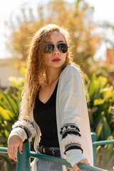 Young woman wearing stylish sunglasses and white sweater in park