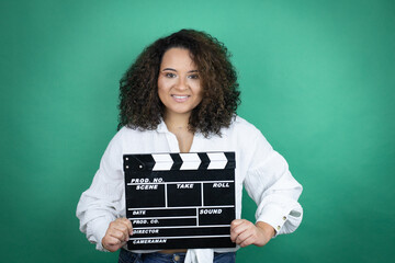 Young african american girl wearing white shirt over green background holding clapperboard very happy having fun