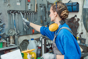 Woman in factory grabbing tool from wall mount